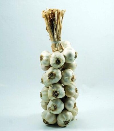 Bir demet Hediyelik Örgü Taşköprü Sarımsağı (3KG) sicimle bağlanmış sarımsak soğanı, düz zeminli hafif bir yüzey üzerinde dik durmaktadır. Sağ üst köşede "act sarımsak" logosu yer almaktadır.