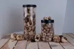 Siyah kapaklı iki şeffaf kavanoz Siyah Sarımsak (200GR) ahşap bir yüzeye yerleştirilmiş, etrafı gevşek sarımsak soğanları ve dişleriyle çevrelenmiştir. Arka plan düz beyazdır.
